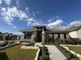 A modern stone-accented home with sleek black-framed windows and lush landscaping in Crosswinds by Highland Homes (Kyle, TX).