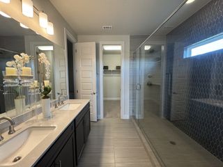 A sleek bathroom featuring a dual sink vanity, modern lighting, and a spacious glass shower with textured tiles.