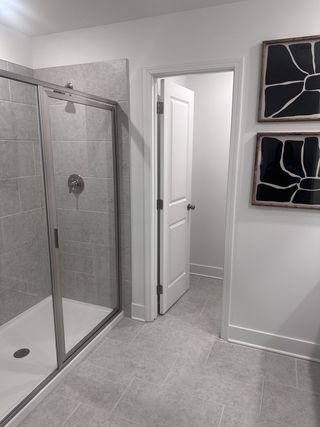 Model Home A sleek bathroom with a glass shower enclosure, light gray tiled walls, and modern art accents.