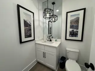 A contemporary bathroom with a sleek black and white vanity, decorative lighting, and stunning framed landscape art.
