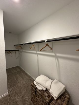 A spacious walk-in closet with ample hanging space, carpeted flooring, and a wicker basket for storage.