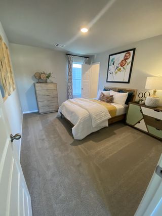 Model Home Cozy bedroom with soft carpet, elegant artwork, a wooden dresser, and warm lighting on a nightstand.