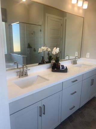 Model Home A modern bathroom featuring a dual vanity, large mirror, and a glass-enclosed shower with elegant tile flooring.