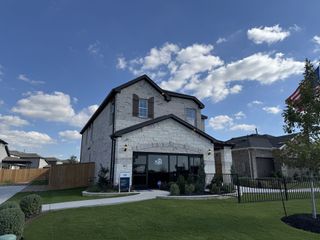 A stunning two-story stone-clad home with wooden shutters and lush landscaping in Crosswinds by Pulte Homes (Kyle, TX).