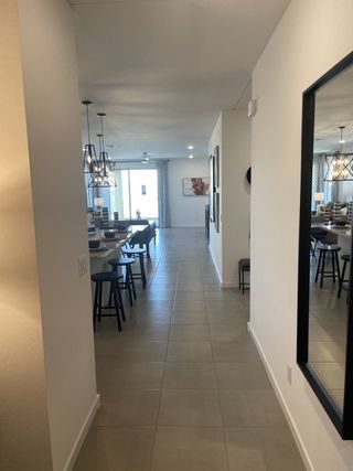A sleek hallway with tiled flooring leads to bright open spaces, featuring contemporary pendant lighting and chic decor.