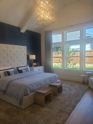 A luxurious bedroom with a tufted headboard, modern chandelier, and large windows providing ample natural light.
