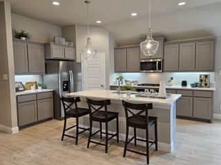 Model Home A modern kitchen featuring gray cabinets, a sleek island with stools, and elegant pendant lighting.