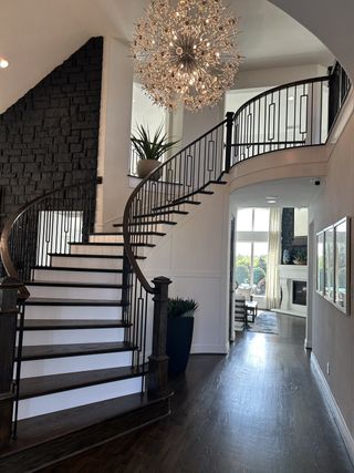 A grand staircase with wrought iron railings, dark wood steps, and a modern chandelier in a spacious foyer.