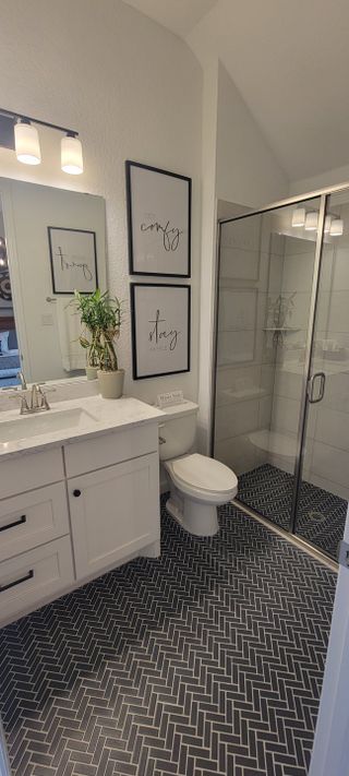 A sleek bathroom with herringbone-patterned flooring, glass shower, white vanity, and modern decor accents.