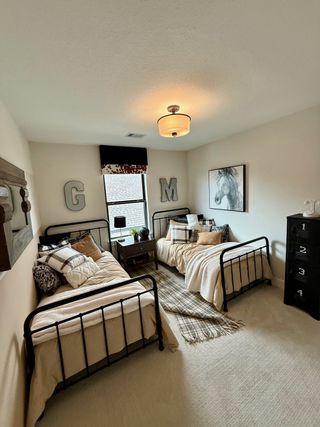 Model Home Cozy bedroom with twin metal beds, plaid accents, and horse art, creating a charming, rustic vibe.