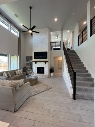 A modern living room with high ceilings, a white stone fireplace, and sleek furnishings. Plenty of natural light and open space.