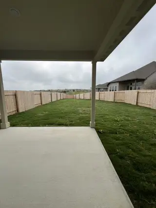 Model Home A covered patio leading to a lush backyard, offering privacy with a tall wooden fence and ample green space.
