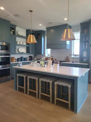 A modern kitchen with blue cabinetry, gold pendant lights, and a large island with woven stools.