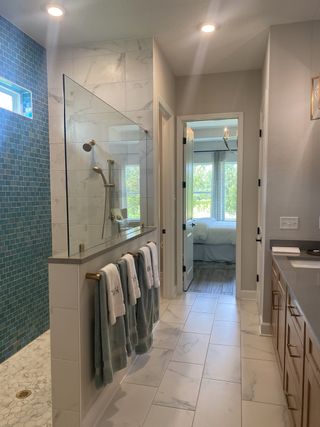 An elegant bathroom with a glass-enclosed shower, marble tiles, and wood cabinetry, leading into a sunlit bedroom.