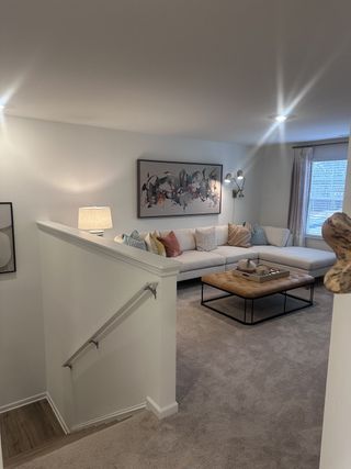 A cozy living room with a plush sectional, modern art, and a tufted coffee table, brightened by ample light and soft decor.