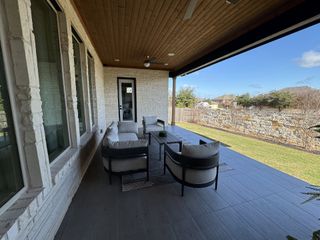 A cozy patio with modern seating and wood ceiling, overlooking a lush backyard and stone fence.