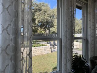 Model Home A serene view through patterned curtains revealing a lush yard and inviting patio seating under a clear blue sky.