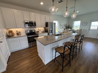 A modern kitchen with granite countertops, white cabinets, stainless appliances, and elegant pendant lighting.