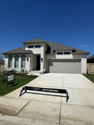 Street view A modern white brick home with sleek black accents and a spacious driveway in Kallison Ranch by Perry Homes (San Antonio, TX).