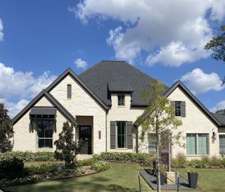 A beautiful stone-accented home with dark trim and lush landscaping in Audubon by Perry Homes (Magnolia, TX).