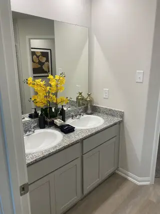 A sleek bathroom features dual sinks with granite countertops, complemented by fresh floral decor and modern cabinetry.