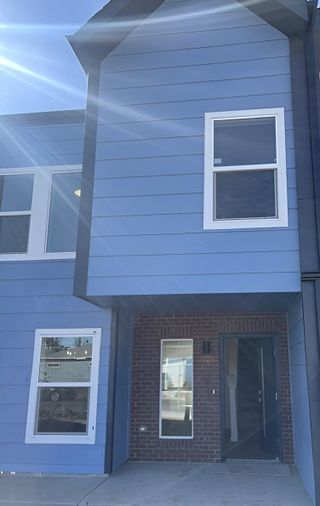 A modern blue townhome with sleek black trim and a brick entry in Grand Ave LiteTowns by RedT Homes (Aurora, CO).