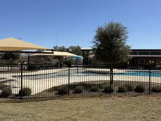 Community Amenities A fenced pool area in Davis Ranch by Pulte Homes (San Antonio, TX) with tan shade sails, a water feature, and a backdrop of clear blue skies.