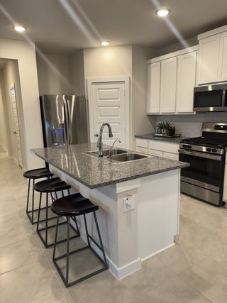 Model Home A modern kitchen with a granite island, stainless steel appliances, and sleek bar stools, offering a stylish cooking space.