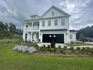 Street view A charming white home with a manicured lawn and porch in Lochton by Mungo Homes (Summerville, SC).