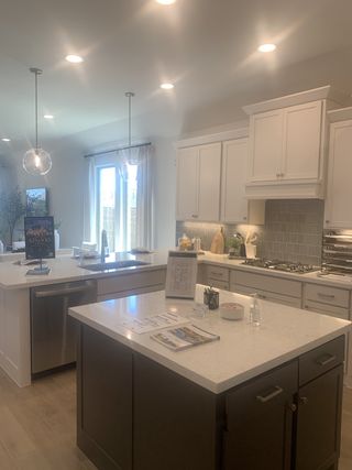 A modern kitchen featuring a sleek island, pendant lighting, and white cabinets with a tiled backsplash.