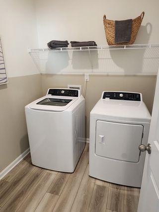 A spacious laundry room with wood-look flooring, overhead shelving, and modern appliances.