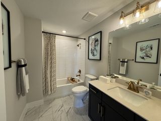 A modern bathroom with marble floors, elegant black vanity, and gold accents, complete with a stylishly curated bath area.