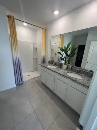 A bright and contemporary bathroom with a double vanity, granite countertops, and a sleek walk-in shower with gradient drapery.
