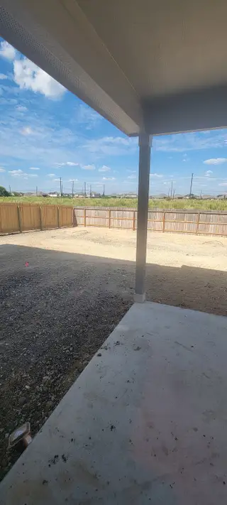 A covered patio overlooking a spacious backyard with a wooden fence under a bright blue sky.