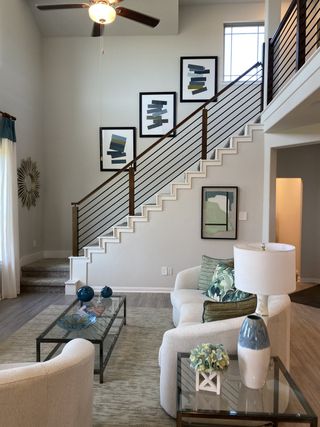 Model Home A contemporary living room with chic decor, abstract art, and a sleek staircase, complemented by elegant seating and glass tables.