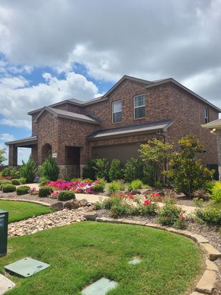 A charming brick home with vibrant landscaping in the Riverfield community by D.R. Horton (Josephine, TX).