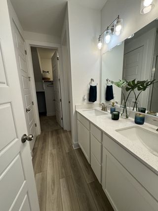 Model Home A sleek bathroom with dual sinks, modern lighting, and laminate wood flooring, leading to a spacious walk-in closet.