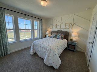 A cozy bedroom featuring a patterned comforter, wall decor, and large windows with ample natural light.
