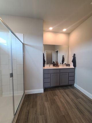 Model Home A modern bathroom featuring a glass-enclosed shower, wooden flooring, and a sleek double-sink vanity with soft lighting.
