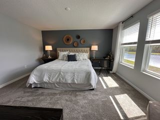 A cozy bedroom with a tufted bed, dark accent wall, dual nightstands, and large windows overlooking a serene pond view.