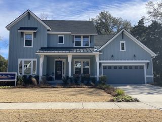 Street view A charming blue home with a welcoming porch and landscaped yard in Norwood Oaks by David Weekley Homes (Mount Pleasant, SC).