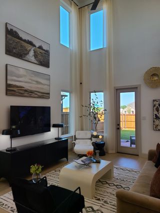 A modern living room with high ceilings, large windows, elegant decor, and a cozy seating area leading to an outdoor patio.