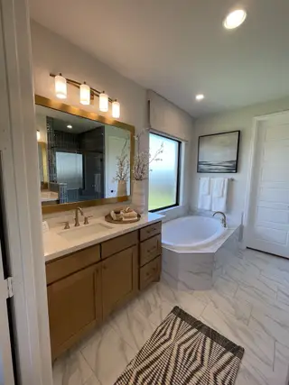 A sleek bathroom featuring a marble-tiled tub, wooden vanity, and elegant lighting with modern decor.