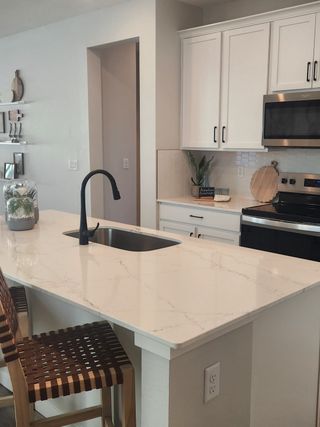 A modern kitchen with a sleek marble island, black faucet, and white cabinetry, complemented by woven barstools.