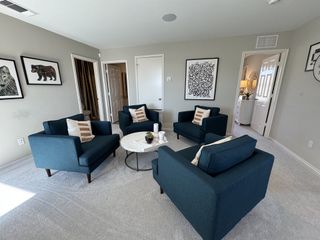 A cozy living room with navy armchairs, abstract wall art, and a round coffee table on a plush carpet.