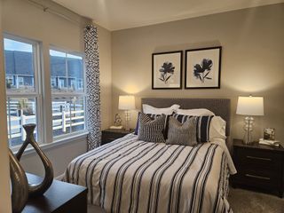 A cozy bedroom with striped bedding, elegant lamps, and floral wall art. Large windows provide natural light and exterior views.