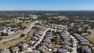 An aerial view of the Caliterra community by Drees Custom Homes in Dripping Springs, TX, showcasing a well-planned neighborhood nestled amidst natural landscapes.
