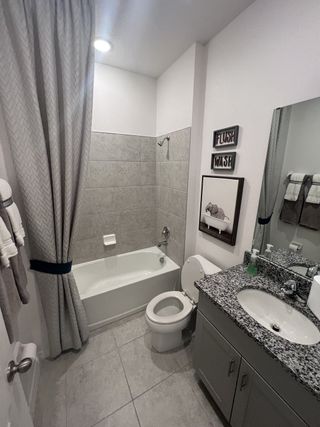 A contemporary bathroom with a sleek granite vanity, tiled bathtub, and soft gray and white tones.

