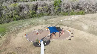 A modern playground with a shaded area surrounded by nature in EastVillage - Classic Collection by KB Home (Manor, TX).