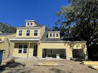 Street view A charming yellow two-story home with a three-car garage in Fiddler Cove by DRB Homes (Mount Pleasant, SC).